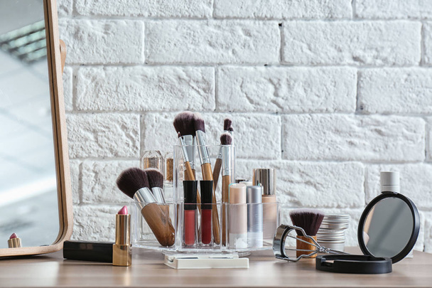 Organizer with cosmetic products for makeup on table near brick wall - Foto, immagini