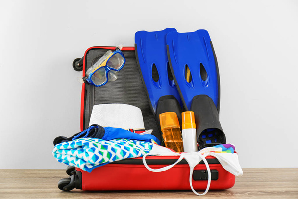 Open suitcase with clothing and swimming accessories on table - Foto, Bild