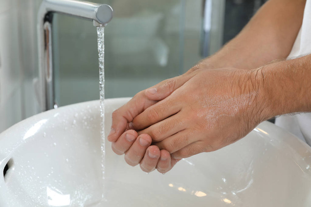 Man washing hands over sink in bathroom, closeup. Using soap - Фото, зображення