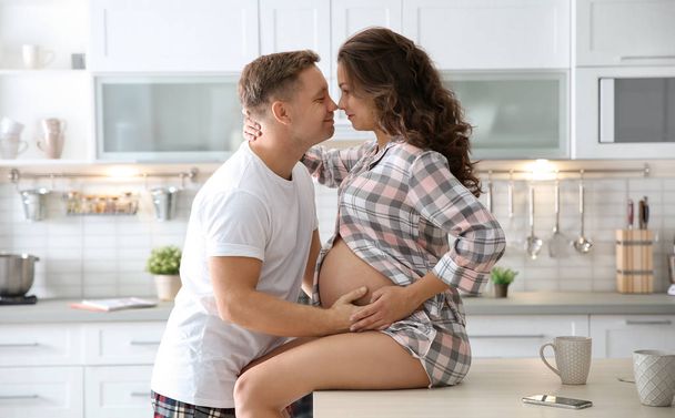 Pregnant woman with her husband in kitchen. Happy young family - Fotó, kép