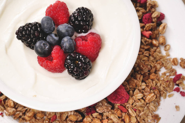 Composition of a typical genuine breakfast made with yogurt, blueberries, raspberries, blackberries, muesli. Concept of: fitness, diet, wellness and breakfasts. - Photo, image