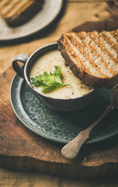 Autumn, Winter home dinner. Fall warming celery cream soup in cup and toast over yellow linen tablecloth, close-up. Comfort food, vegan, vegetarian, healthy and slow food concept - Foto, Imagem