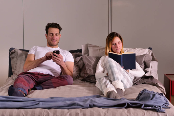 A married couple in bed use the phone separately to send messages or use social networks and no longer talk to each other. Concept of: new generations, separation, technology. - Foto, imagen