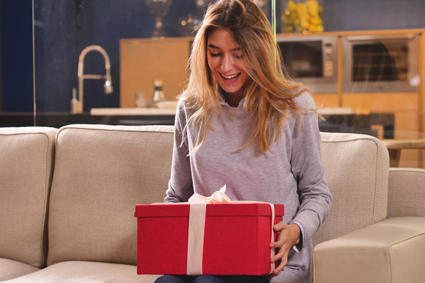Девушка дома открывает подарочный пакет, который прибыл. Пакет может быть подарком или заказ прибыл благодаря интернет-магазинам. Понятие: шоппинг, любовь, подарок, юбилей
. - Фото, изображение