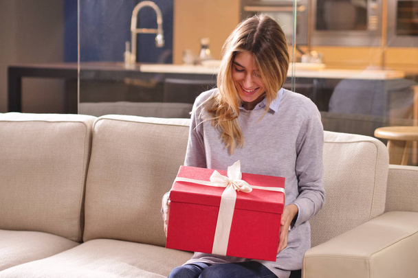 Une fille à la maison ouvre un sac cadeau qui est arrivé. Le paquet peut être un cadeau ou une commande est arrivé grâce à des achats en ligne. Concept de : shopping, amour, cadeau, anniversaire
. - Photo, image