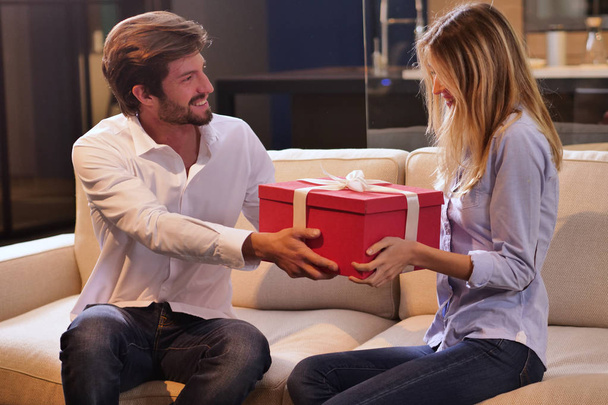 A man gives his own gift to his boyfriend as a sign of love for their anniversary. The girl is happy with the surprise she has just received. Concept of: gift, love, valentine's day, anniversary. - Photo, image