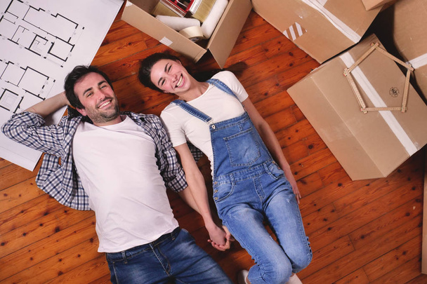 couple in love lying on wooden floor with room plan, cardboard boxes and rulers - Photo, Image