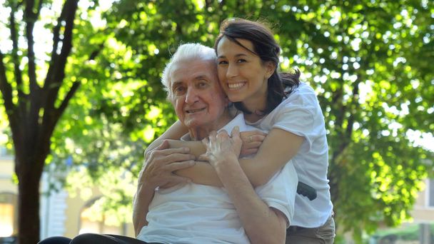 Neta, enfermeira, cuidando dos idosos, menina (mulher) abraçando o avô, sorrindo, feliz, andando no parque. Conceito: pensão, sanatório, uma casa para idosos, ajuda para os idosos
. - Foto, Imagem