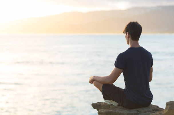 Młody mężczyzna ocean zachód słońca podczas wykonywania jogi medytacji. Relaks i odbicie. - Zdjęcie, obraz