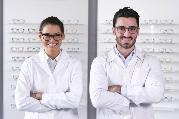 two ophthalmologists woman and man in optical shop with arms crossed - Foto, afbeelding