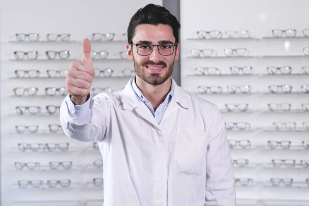 handsome Caucasian man wearing eye glasses in optical center and gesturing thumbs up  - Φωτογραφία, εικόνα