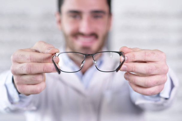 Portrait of smiling ophthalmologist man showing glasses to camera  - Фото, зображення