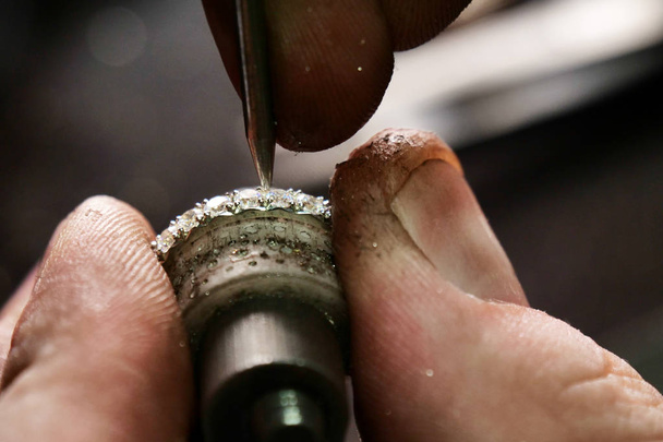 Close up of a goldsmith's hand making a gold or silver ring or a diamond using goldsmith's tools. For this work it takes precision and patience. Concept of: tradition, luxury, jewelry. - 写真・画像