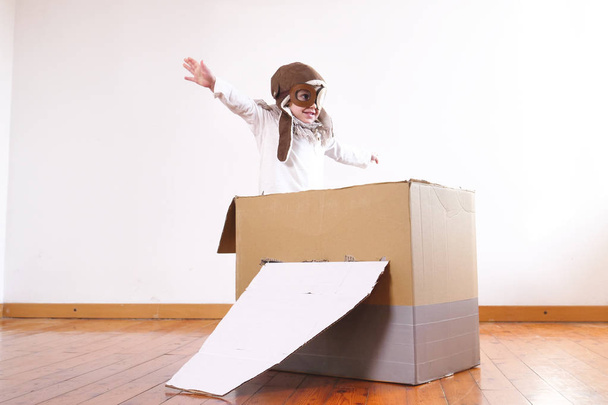 happy adorable little girl dressed as pilot playing in handmade cardboard box plane  - Fotó, kép
