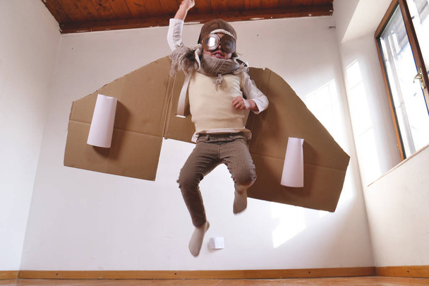 playful little boy dressed as aviator pilot in handmade cardboard box plane  - Фото, зображення