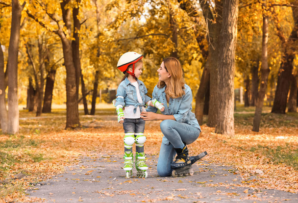 Mother and her daughter wearing roller skates in autumn park - Zdjęcie, obraz