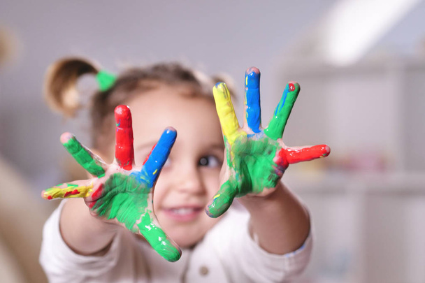 Portrait of a little girl in her bedroom showing her hands all colored with paint. Concept of: color, creativity, art, happiness and educational. - Photo, Image