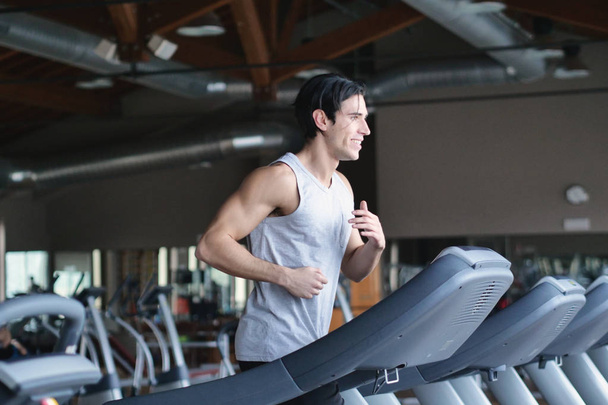 handsome brunette  caucasian man running on treadmill in gym  - 写真・画像