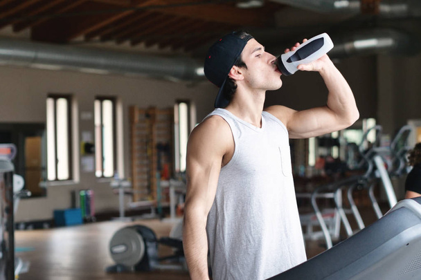 man during break drinking water from bottle while standing in gym  - Fotó, kép