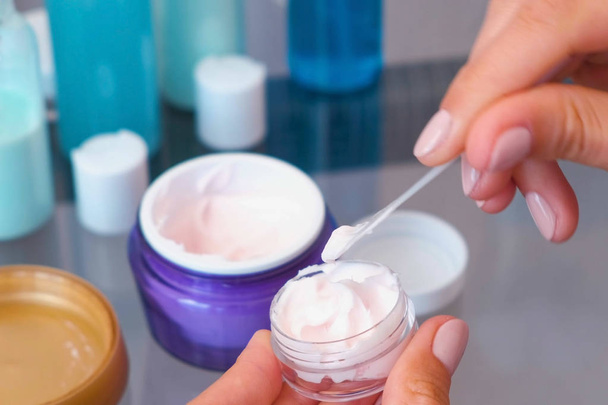 Womens hands put the cream from a large jar into a small one with a spatula. Road set of cosmetics. Close-up. - Foto, Imagem