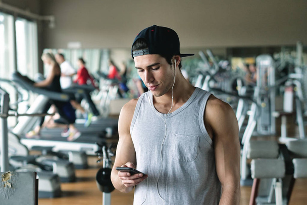 Portrait of a guy in a gym getting ready for his workout and putting some music on his headphones to charge himself with power. Concept of: sport, personal trainer and fitness and music - Foto, Imagem