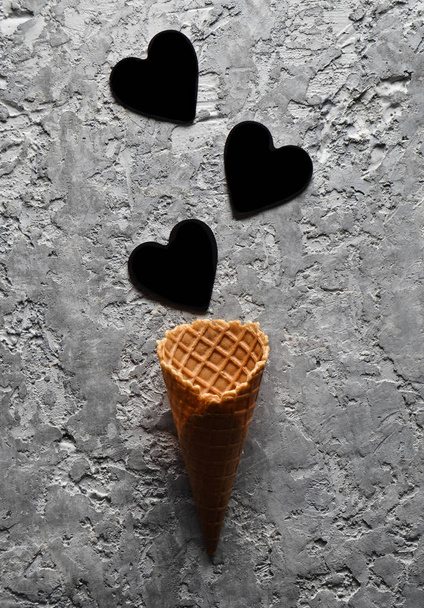 Пустой вафельный рог и черные сердца на сером бетонном фоне, минималистский тренд, верхняя борьба
 - Фото, изображение