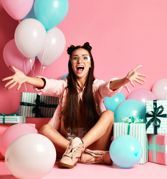 Beauty girl with colorful air balloons and gift boxes laughing. she happily screams sitting on the floor and looks into camera - Foto, Bild