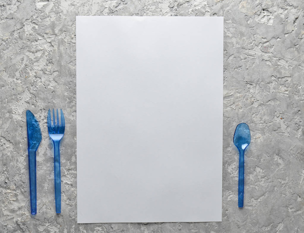 Λευκό φύλλο χαρτί για διάστημα αντίγραφο, πλαστικό μαχαίρι, κουτάλι και πιρούνι σε ένα γκρι επιφάνεια σκυροδέματος. Έννοια των τροφίμων. Κορυφή vie - Φωτογραφία, εικόνα