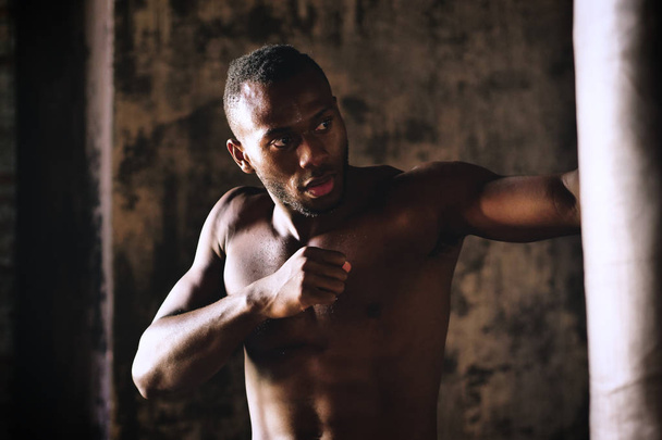 schöner hemdloser muskulöser afrikanischer Mann boxt Boxsack  - Foto, Bild