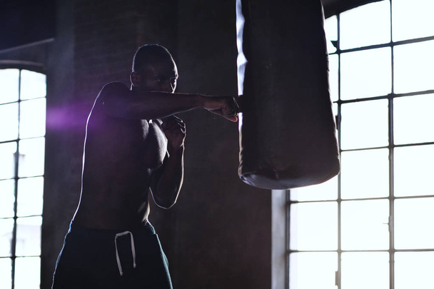 handsome shirtless muscular african man boxing punching bag  - Фото, зображення