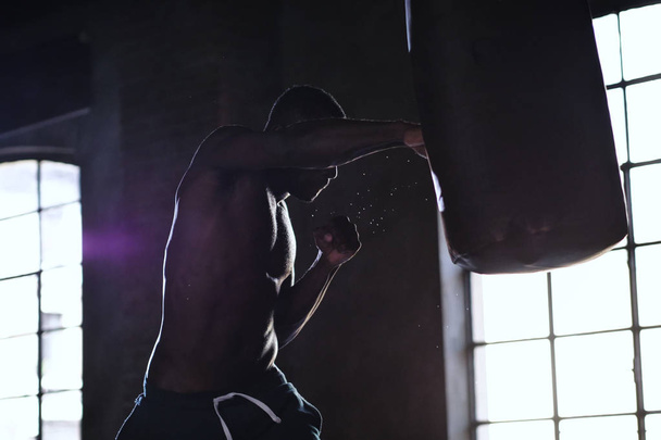 handsome shirtless muscular african man boxing punching bag  - Фото, изображение