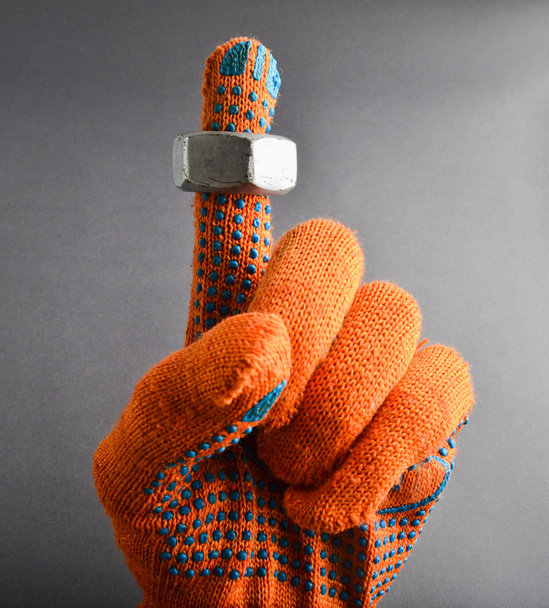 灰色背景がある上にオレンジ色の作業手袋と手の人差し指に金属のナット - 写真・画像