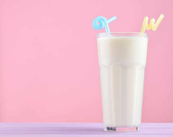 A glass of milkshake with a straw on a pastel color wooden table isolated on pink. Copy spac - Photo, Image