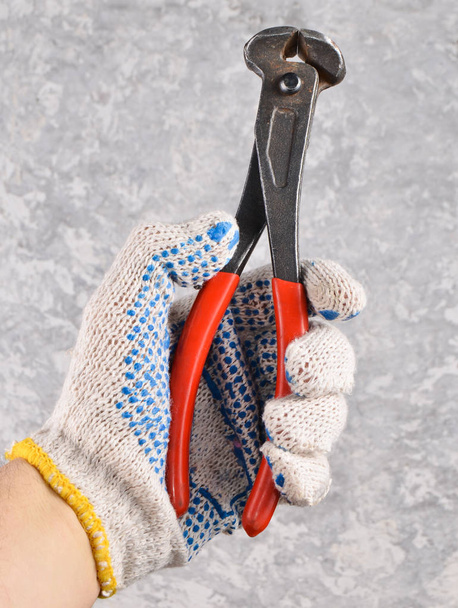 Mužská ruka s rukavicemi drží kovové kleště proti šedé betonové poza - Fotografie, Obrázek