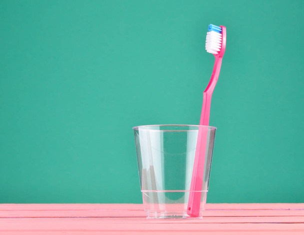 ミントの緑のパステル背景、ミニマルなトレン透明カップでピンクの歯ブラシ - 写真・画像