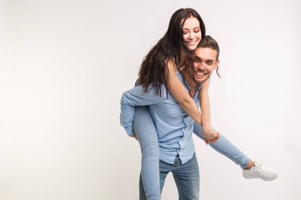 Divertimento e conceito de relacionamento - Homem carregando namorada de costas no fundo branco
 - Foto, Imagem