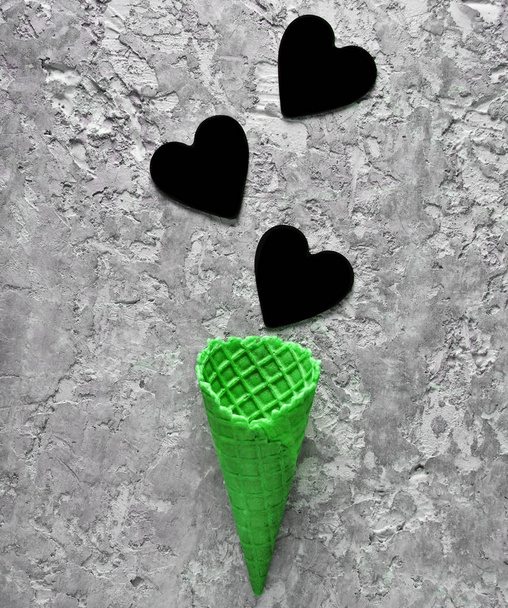 Lege groene wafel hoorn en zwarte hartjes op een grijze concrete achtergrond, minimalistische trend, top wedijveren - Foto, afbeelding