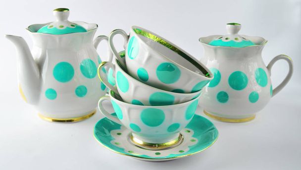 Пачка старинных керамических чашек на блюдце, чайники, сахарные чашки на белой спинке
 - Фото, изображение