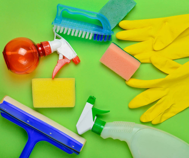 Produits de nettoyage pour maison. Vadrouille, éponge, flacon de spray, gants en latex jaune, brosse sur fond vert. Vue de dessus. Pose plate styl
 - Photo, image