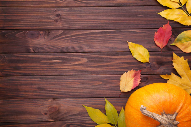 Оранжевая тыква с красными и оранжевыми листьями на коричневом фоне. День благодарения
 - Фото, изображение