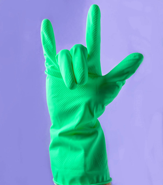 Egy sárga gumi kesztyűt kezét felbukkan egy rock-kürt, két ujjal a kék háttere - Fotó, kép