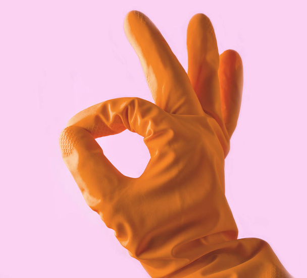 Hand in gele rubberen handschoenen geeft duimen symbool oke op roze achtergrond. - Foto, afbeelding