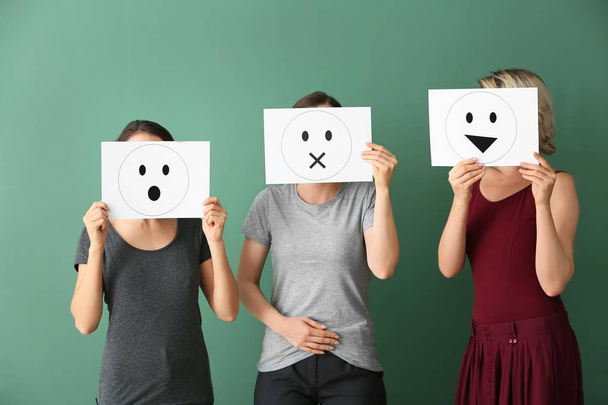 Jovens mulheres escondendo rostos atrás de folhas de papel com emoticons desenhados em fundo de cor
 - Foto, Imagem