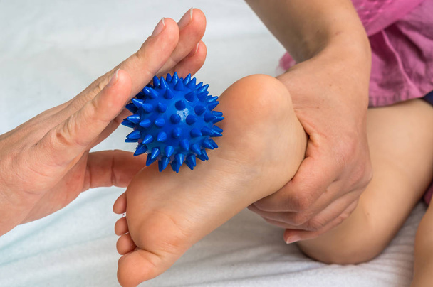 Mother makes foot massage to her baby with blue massage ball - Photo, Image