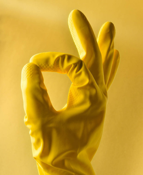 Рука в жёлтых резиновых перчатках показывает символ большого пальца на красном фоне
. - Фото, изображение