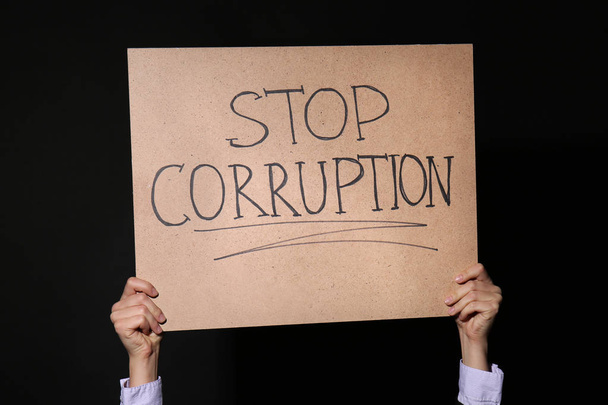 Frau hält Plakat mit Text Stop Korruption auf schwarzem Hintergrund - Foto, Bild