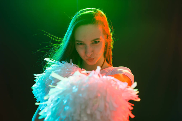 Tanz, Cheerleading und People-Konzept - junges Mädchen im Dunkeln unter buntem Licht mit Bommeln auf dem Kopf - Foto, Bild