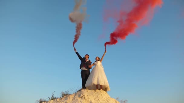 Šťastná nevěsta a ženich mává barevné růžový kouř proti modré obloze a směje se. Líbánky. Romantiku. Vztah mezi mužem a ženou - Záběry, video