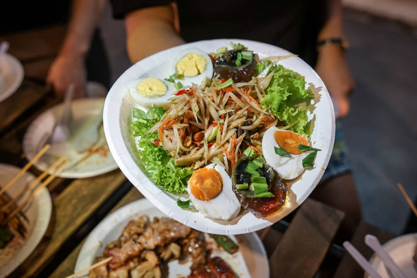 Somtum; Salada de mamão picante com peixe em conserva em prato de papel no evento de comida de rua foodtruck., Bangkok, Tailândia
. - Foto, Imagem