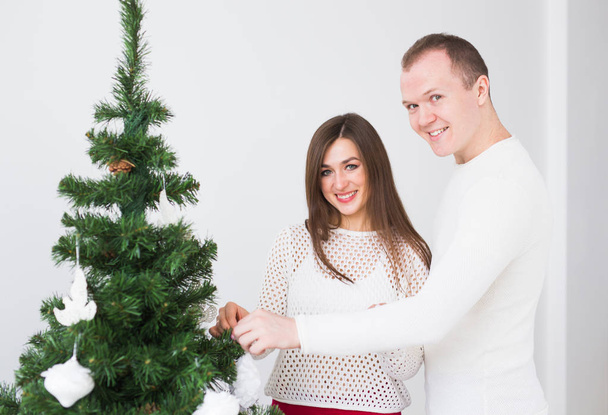 Winter holidays concept - Happy love couple decorating Christmas tree in the room - Photo, Image